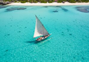 Safari Blue Sansibar - Traditionelles Dau-Segelboot mit dreieckigem Segel auf kristallklarem, blauem Wasser mit Touristen an Bord während der Safari Blue Tour.