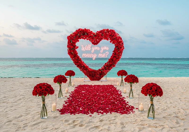 A romantic proposal setup on a Zanzibar beach featuring a large heart-shaped arrangement of red roses.